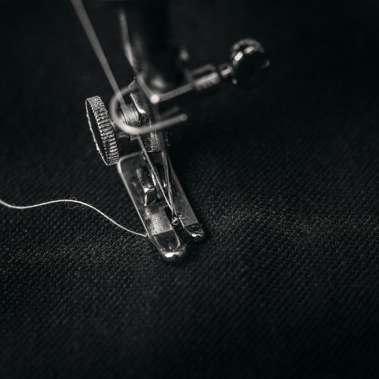 Dettaglio di macchina da cucire durante la lavorazione di abbigliamento sportivo NOAK SPORT su tessuto nero